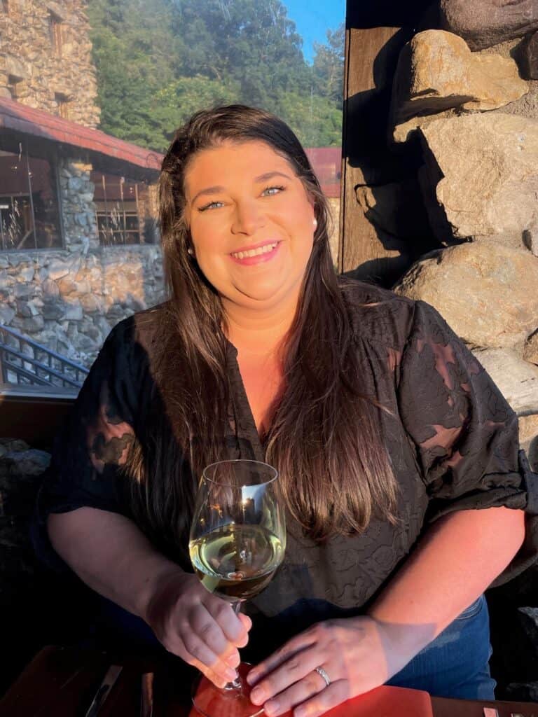 Chloe Green smiling and holding a glass of white wine outdoors