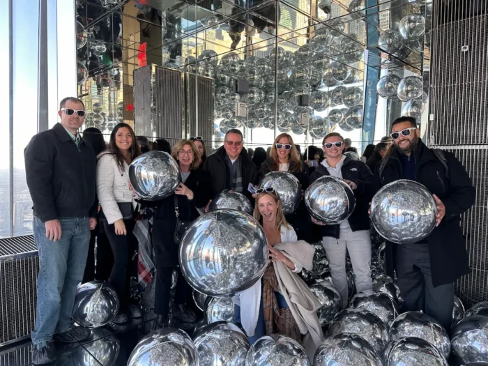 A Team associates out on a group outing wearing white sunglasses and holding large silver circle balloons
