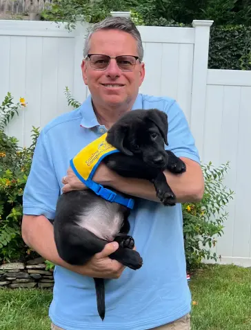 Man holding a Canine Companion black puppy.