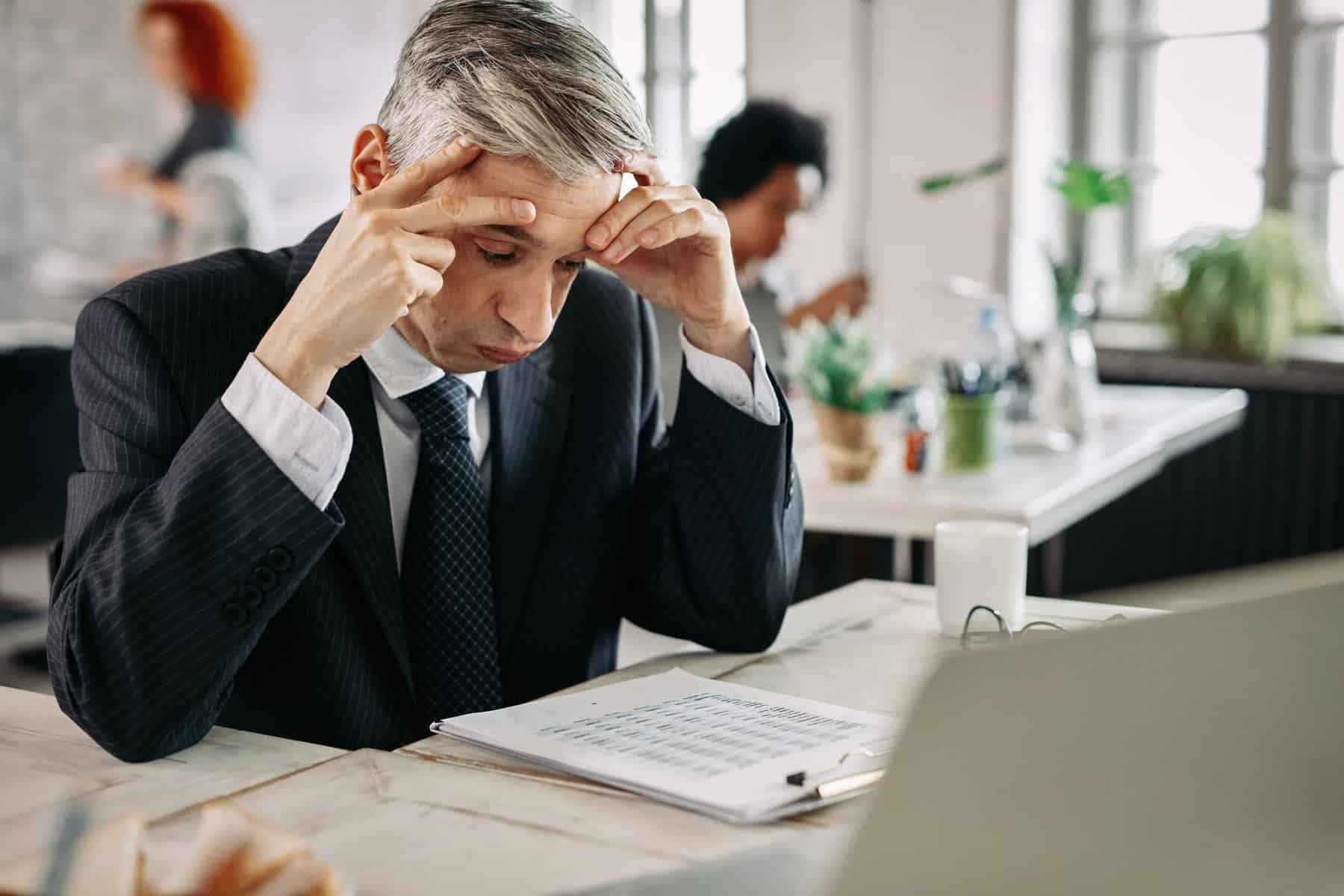 businessman feeling stressed while reading problematic financial reports