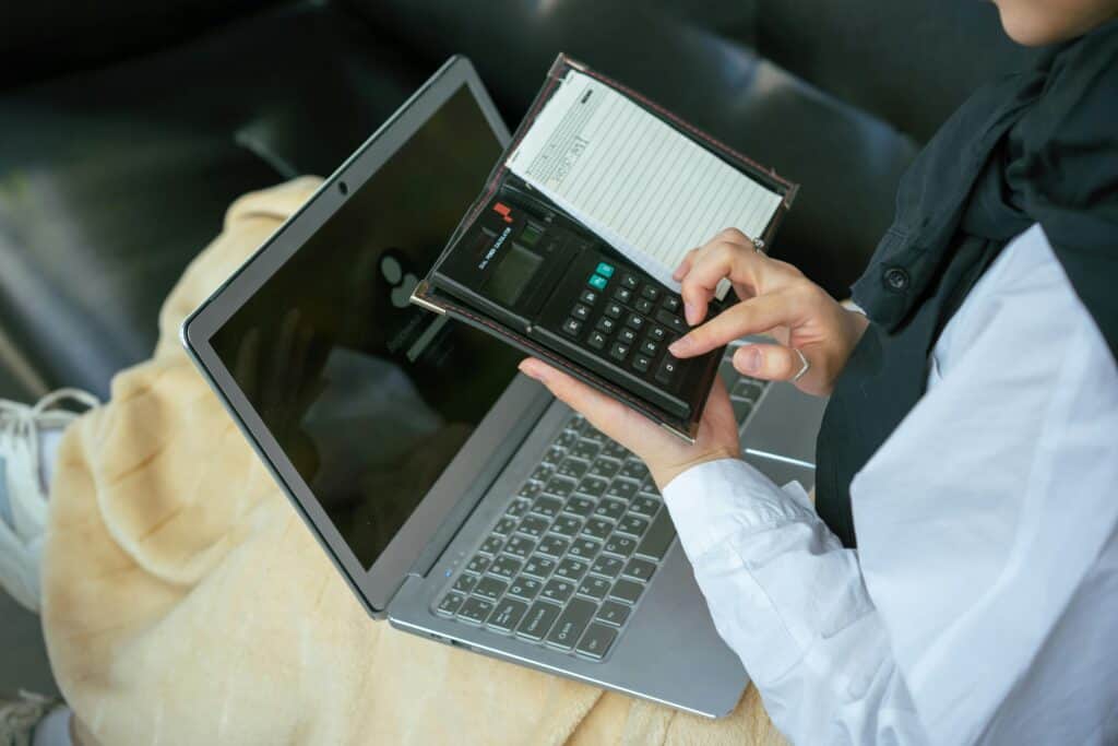 A Person with Laptop on Her Computing Something on the Calculator