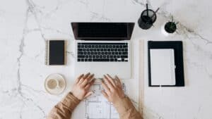 Person in Brown Long Sleeve Shirt Using Macbook Pro Beside White Ceramic Mug